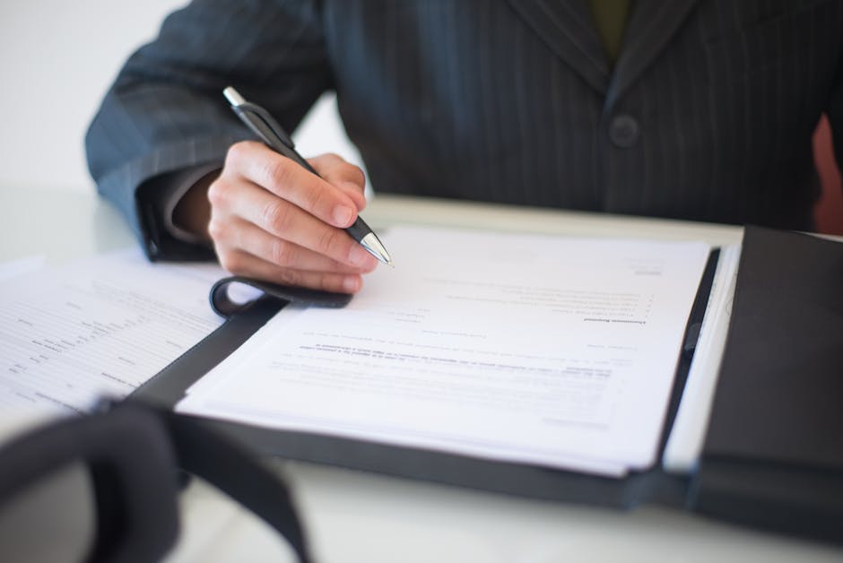 Businessperson signing compliance form with pen at desk