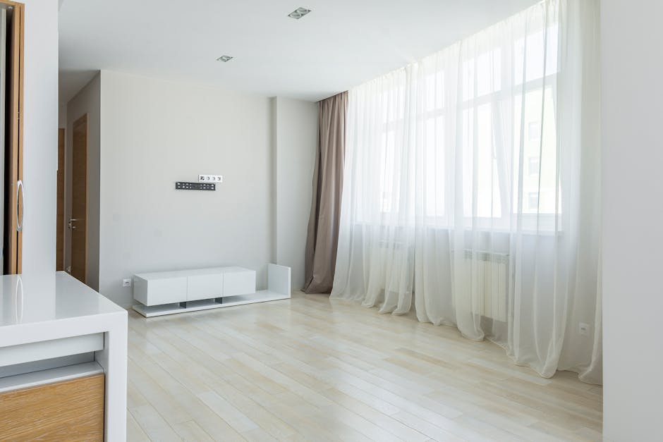 empty modern living room with large windows and sunlight streaming through curtains
